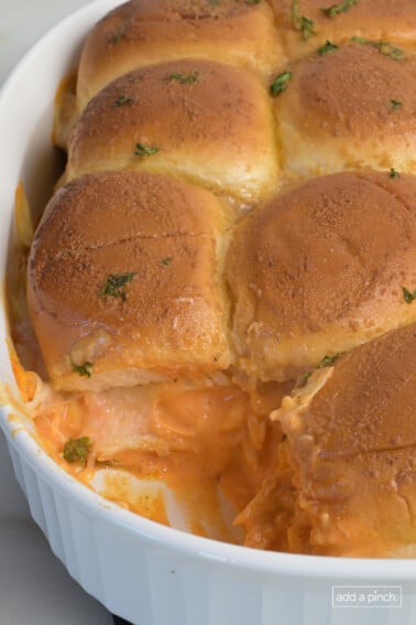 Buffalo chicken sliders in a baking dish topped with a buttery spread.