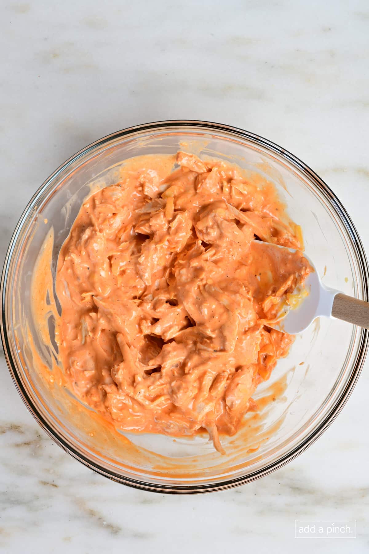Ingredients for buffalo chicken sliders mixed together in a glass bowl.