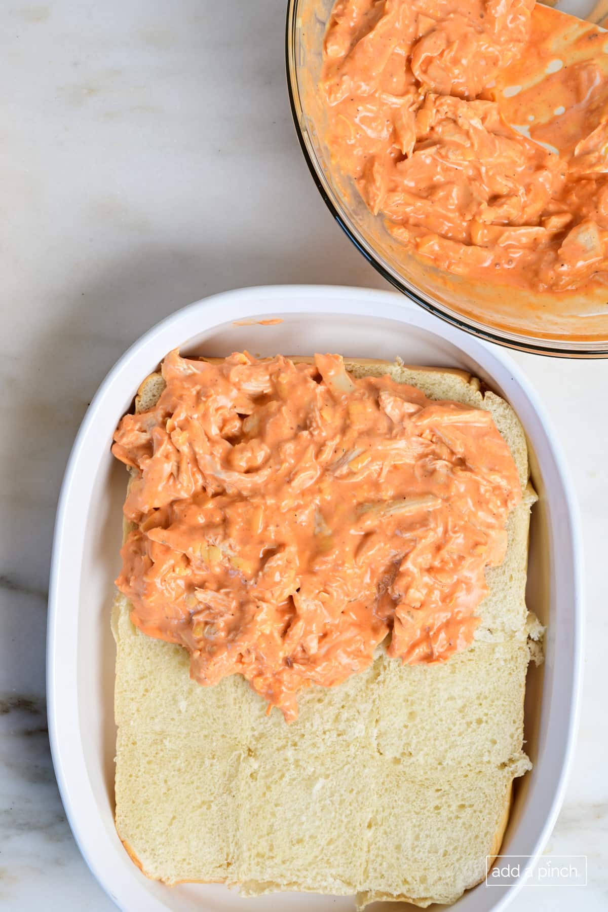 Buffalo chicken sliders filling being spread onto bottom half of butter rolls.