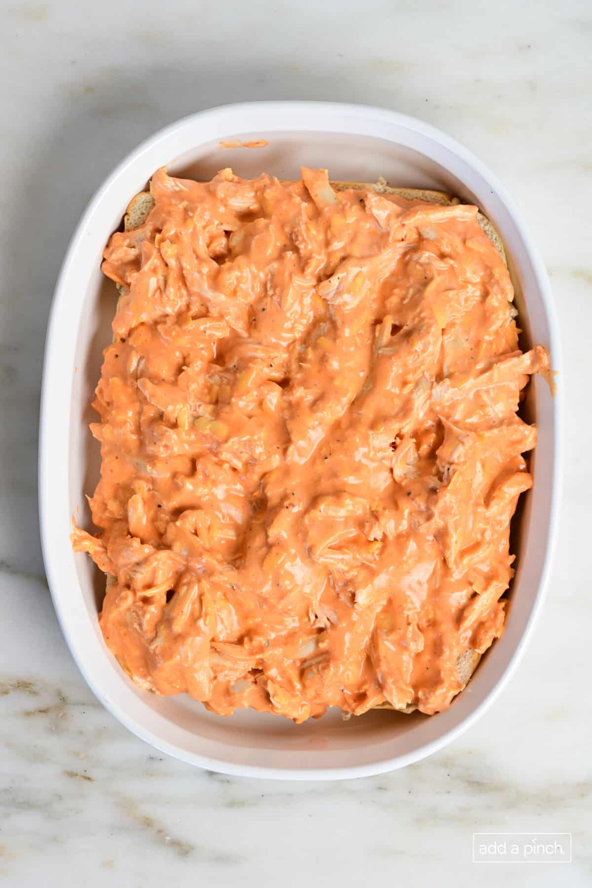Buffalo chicken slider filling on buttery rolls in baking dish.