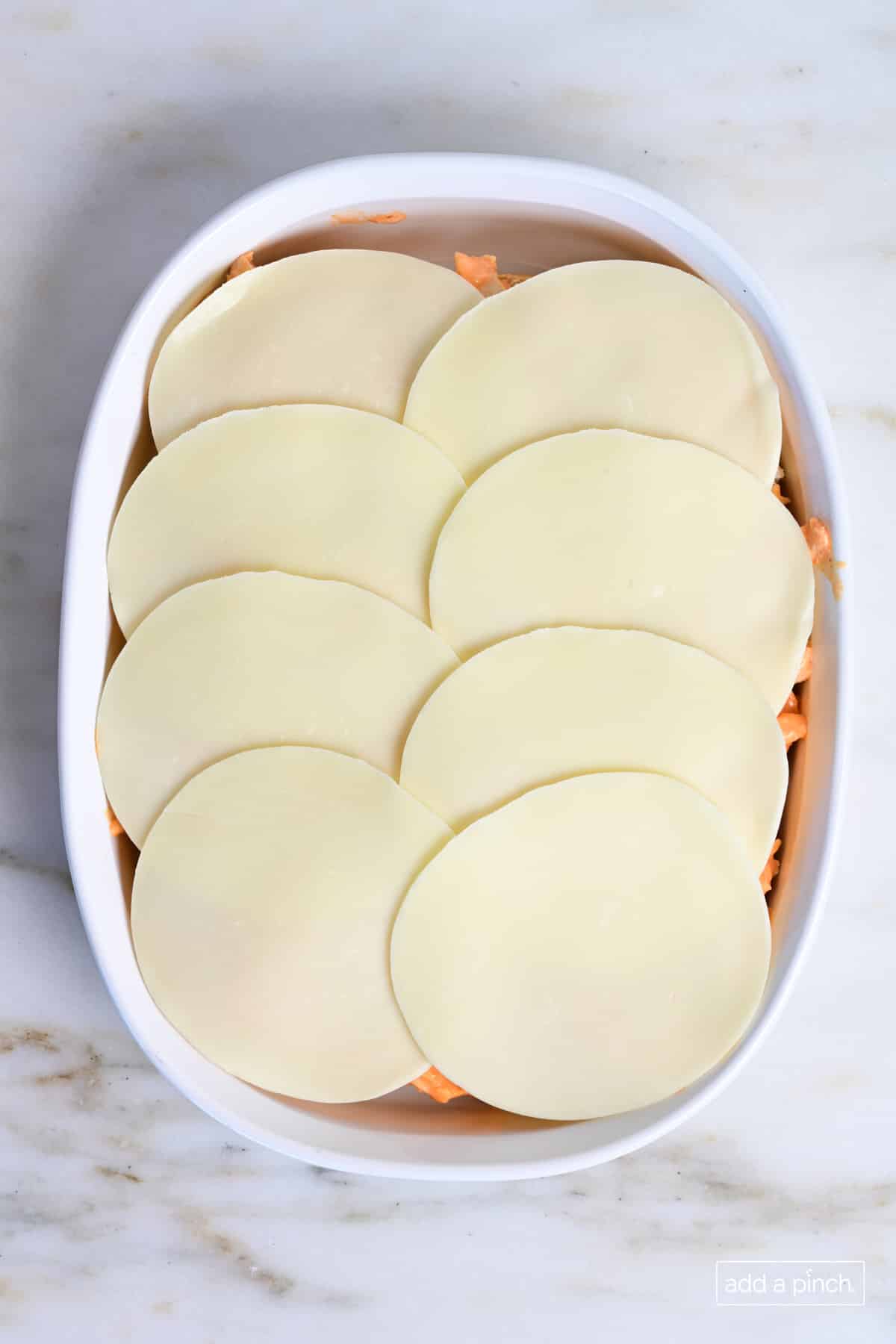 Provolone cheese slices on top of buffalo chicken slider filling.