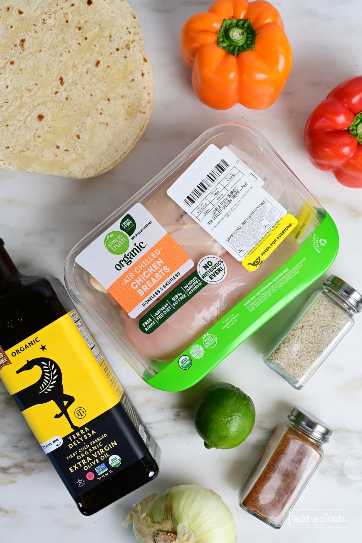 Ingredients for chicken fajitas - chicken breasts, olive oil, peppers, spices, onion, lime, and tortillas.