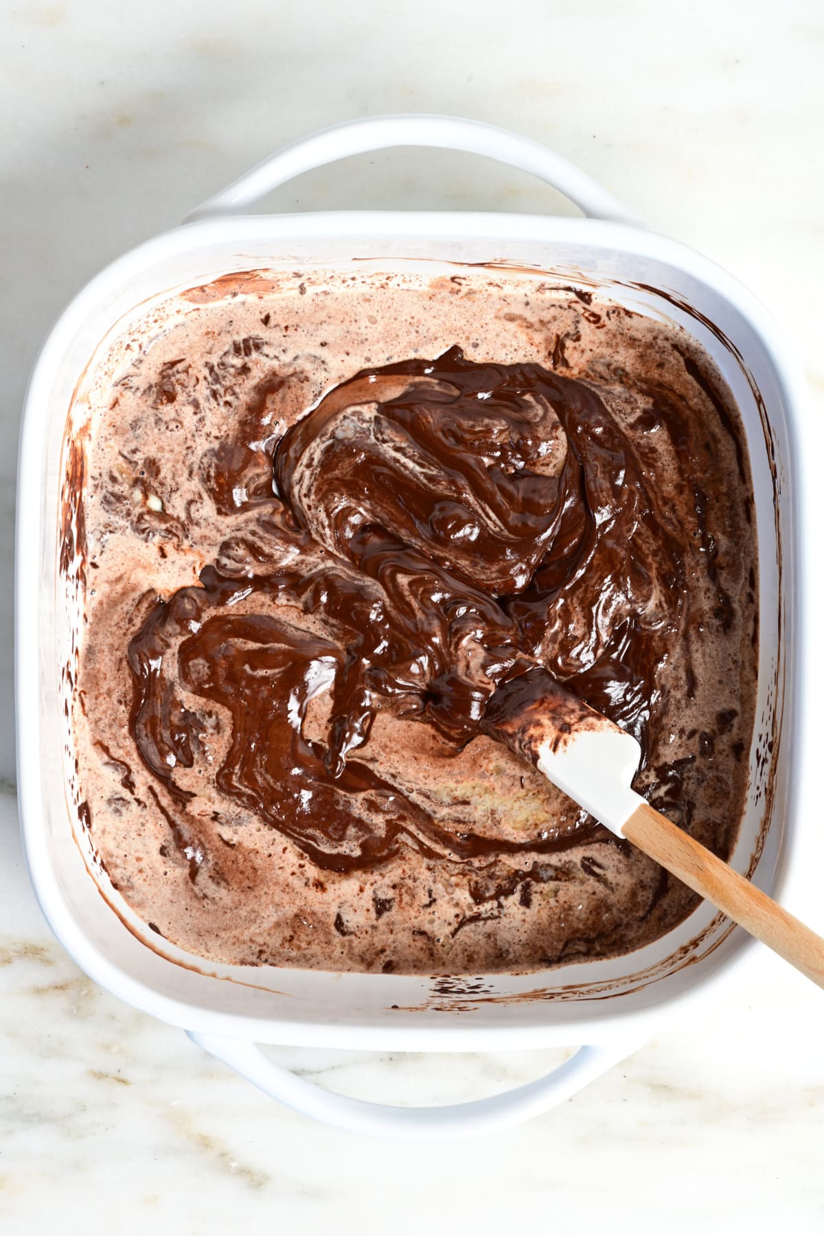 White spatula stirring ganache in a white baking dish.