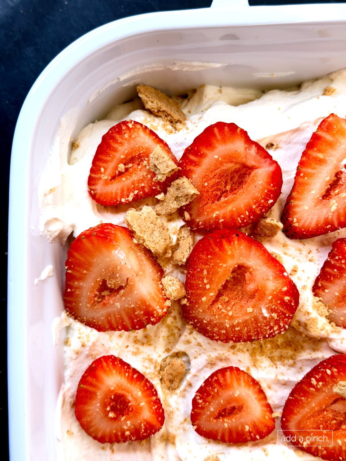 Close-up of a beautiful no-bake Strawberry Icebox Cake in a white 9x13 baking dish, topped with fresh sliced strawberries over fluffy homemade whipped cream. This easy summer dessert features layers of graham crackers that soften into cake-like perfection.