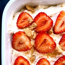 Close-up of a beautiful no-bake Strawberry Icebox Cake in a white 9x13 baking dish, topped with fresh sliced strawberries over fluffy homemade whipped cream. This easy summer dessert features layers of graham crackers that soften into cake-like perfection.