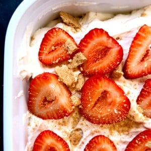 Close-up of a beautiful no-bake Strawberry Icebox Cake in a white 9x13 baking dish, topped with fresh sliced strawberries over fluffy homemade whipped cream. This easy summer dessert features layers of graham crackers that soften into cake-like perfection.