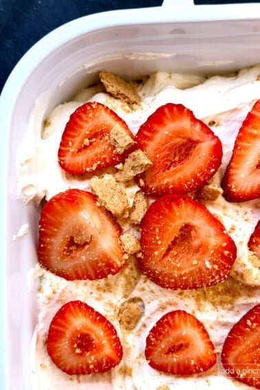Close-up of a beautiful no-bake Strawberry Icebox Cake in a white 9x13 baking dish, topped with fresh sliced strawberries over fluffy homemade whipped cream. This easy summer dessert features layers of graham crackers that soften into cake-like perfection.