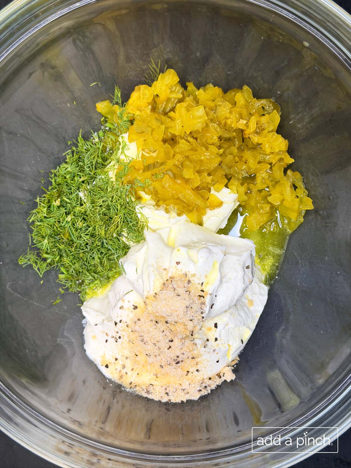 Softened cream cheese, sour cream, chopped dill pickle chips, fresh dill, Stone House Seasoning, and hot sauce in a mixing bowl for creamy dill pickle dip.