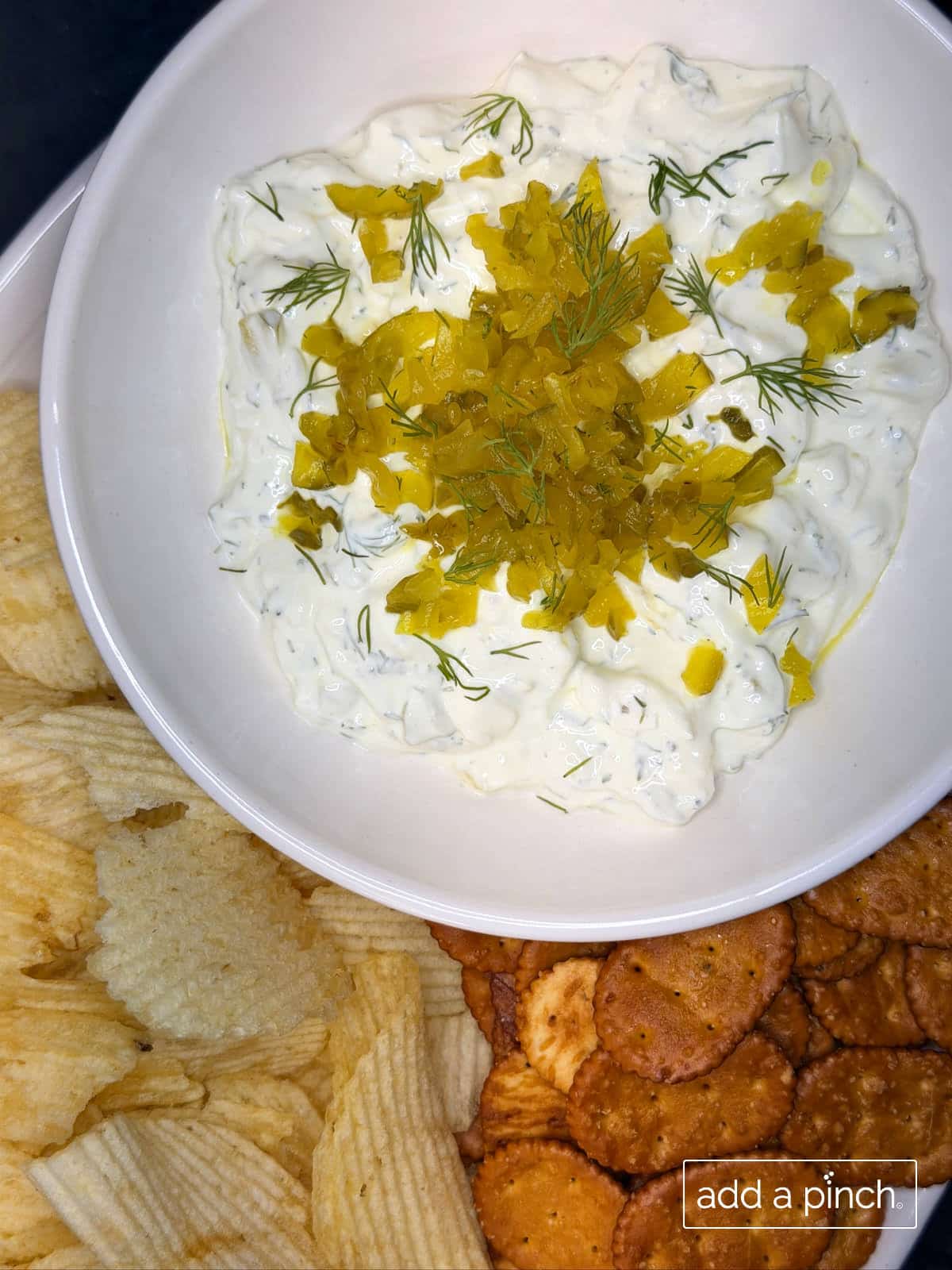 Dill pickle dip served with ruffled potato chips, pretzels, and fresh veggie sticks on a sunny outdoor table perfect for summer lake days or game day.