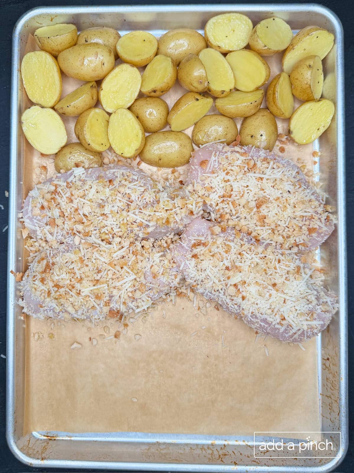 Parmesan crusted chicken on a baking sheet with baby potatoes ready to bake.
