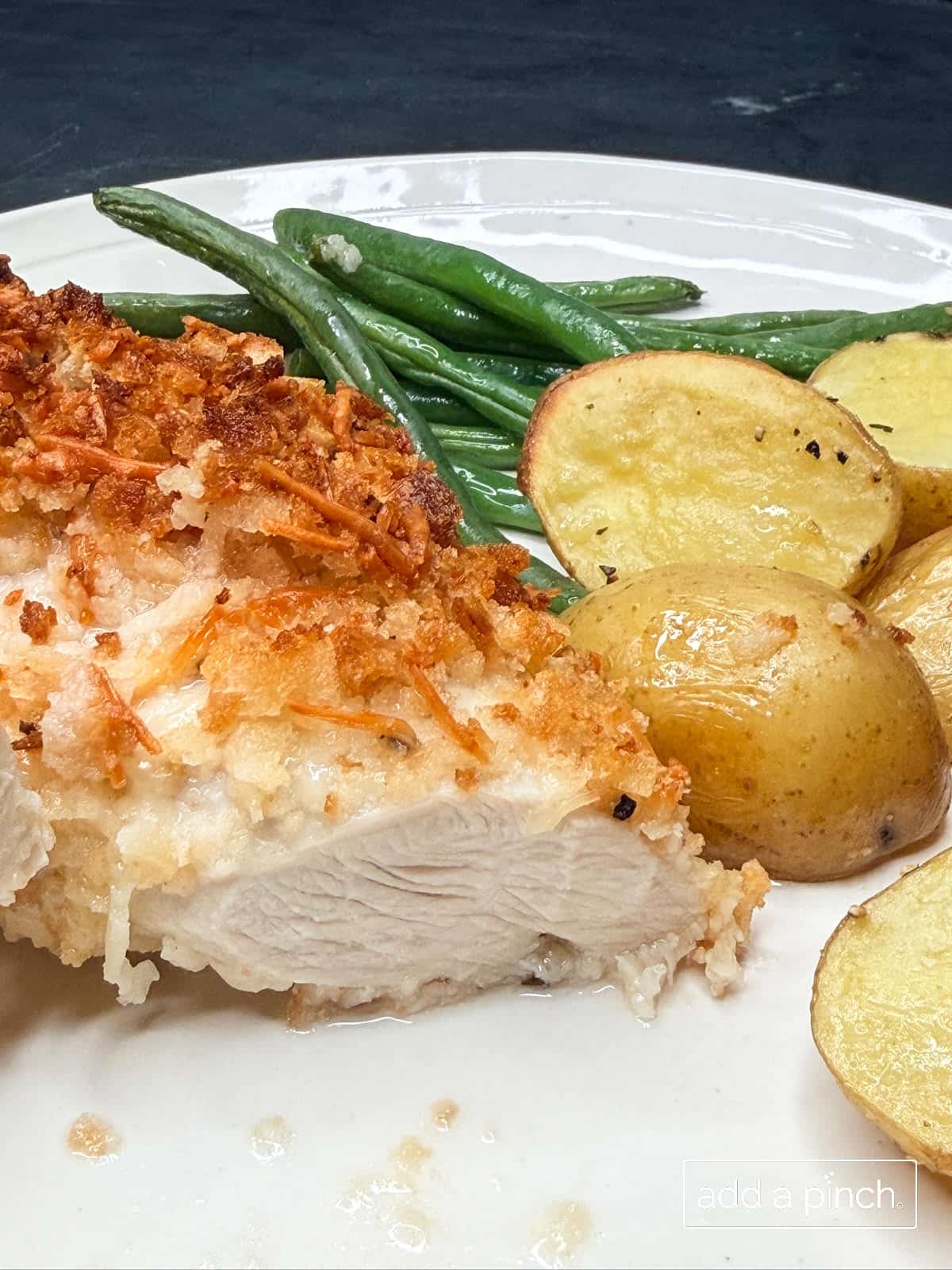 Parmesan crusted chicken with baby potatoes and green beans on a white plate.