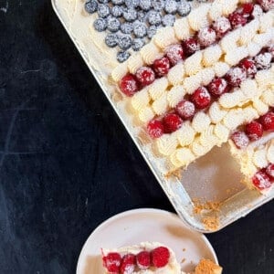 Sugar Cookie Flag Cake in a half sheet pan topped with cream cheese or buttercream frosting and fresh blueberries and raspberries arranged as an American flag