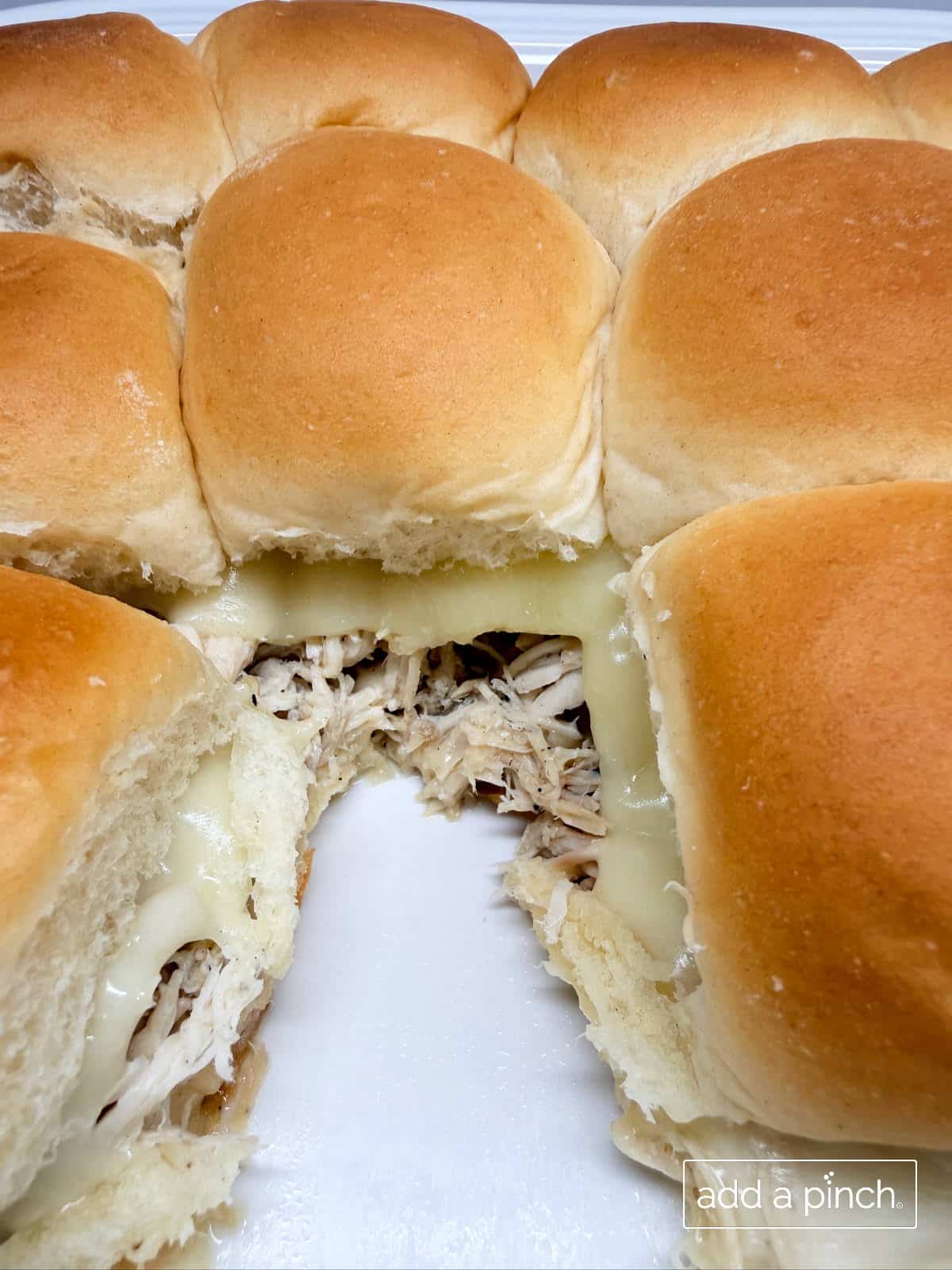 Mississippi chicken sliders with shredded pepperoncini chicken and melted provolone cheese in baking dish.